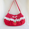 A red shoulder bag with white polka dot fabric on the top, white ruffle trim, a white drawstring bow, and a strawberry applique on the front, set against a plain white background.